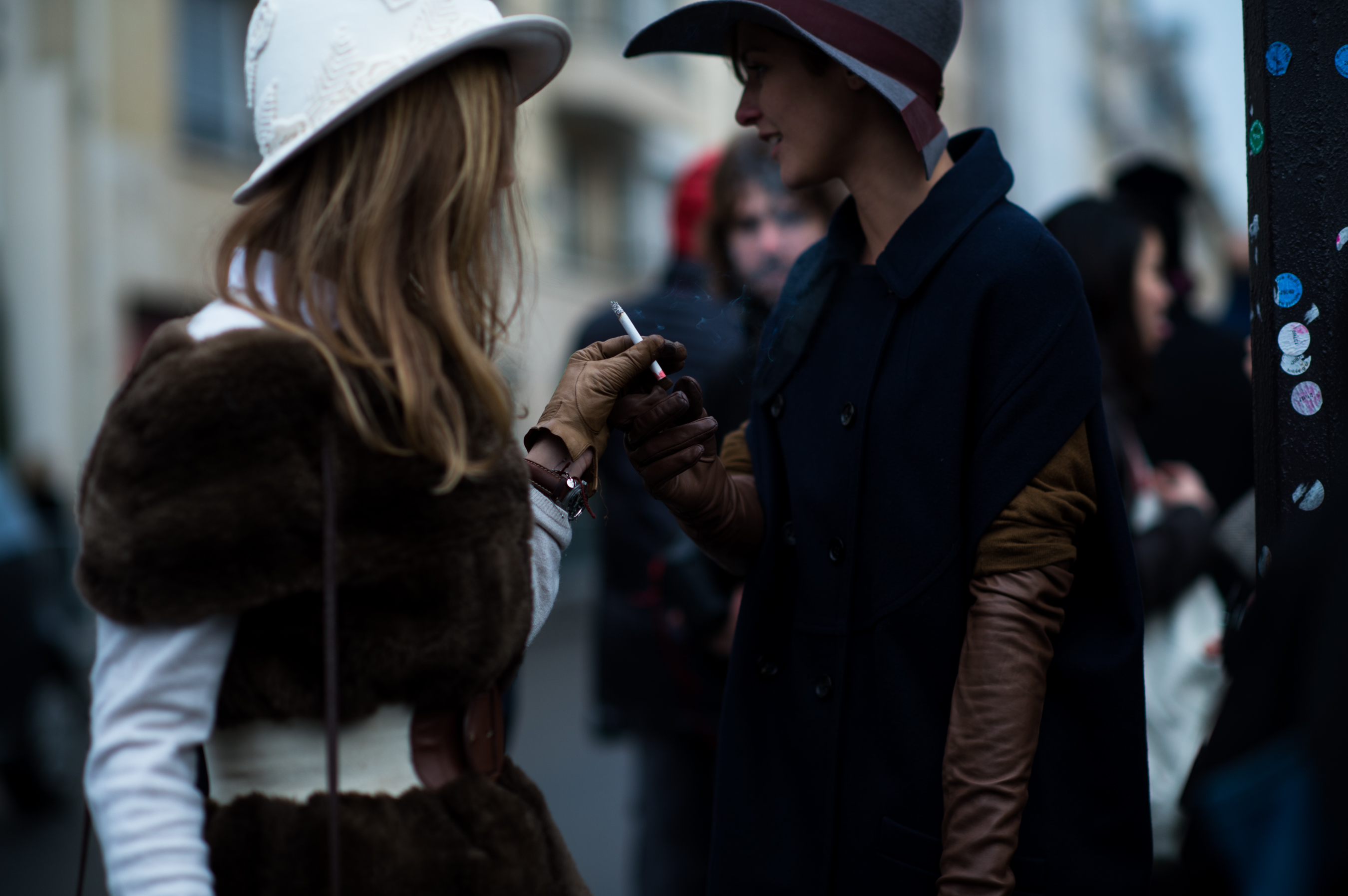 Two women in hats sharing a cigarette