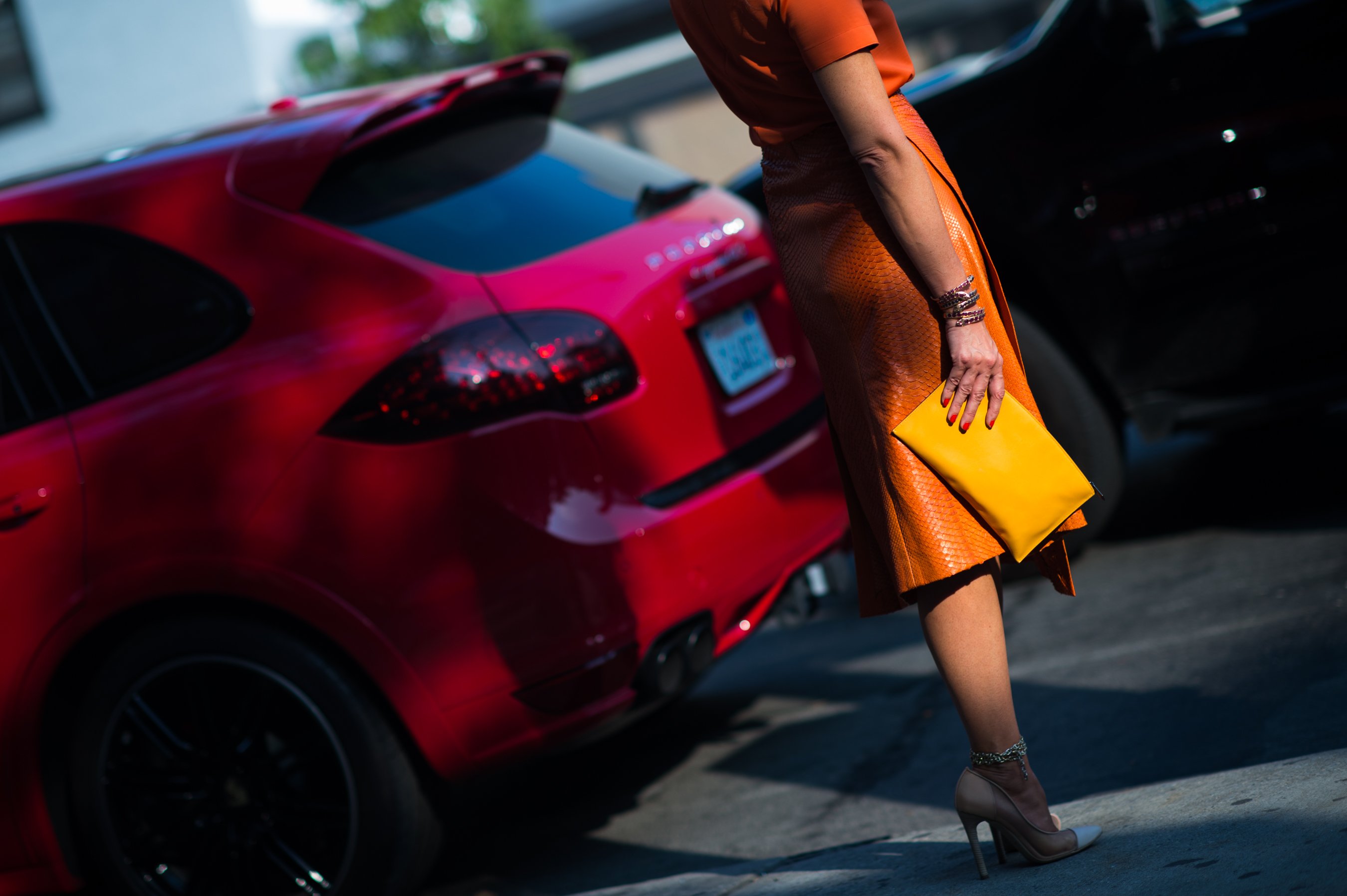 Woman wearing orange next to a red Porsche