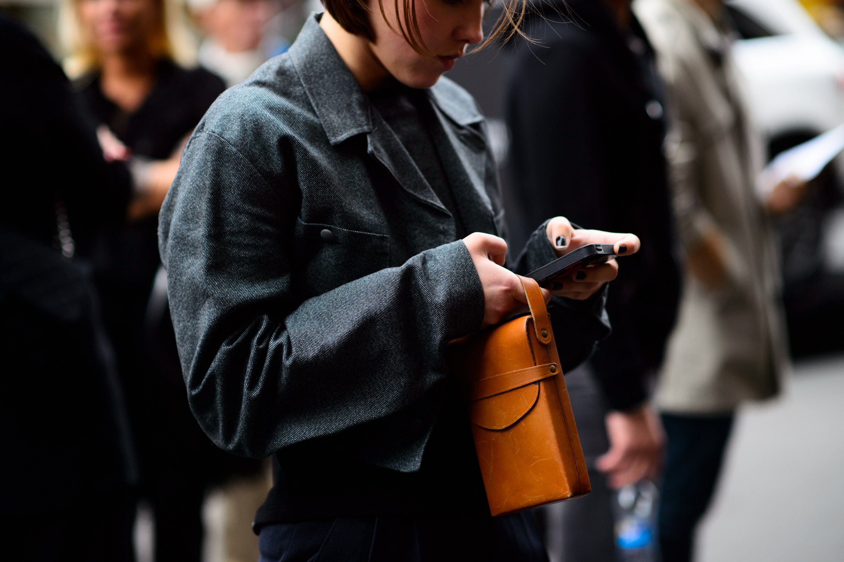 Woman in grey jacket with orange bag texting