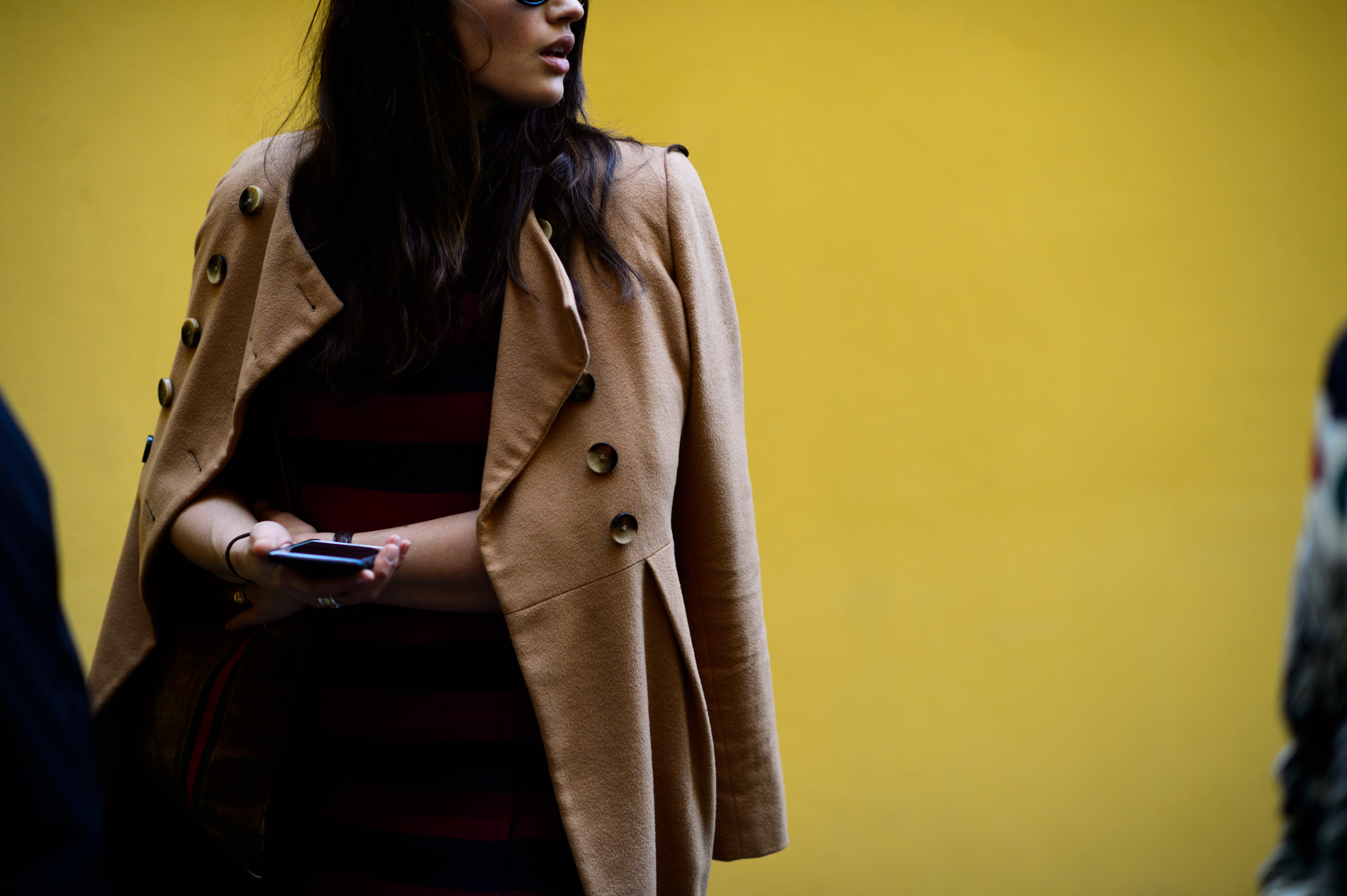 Woman wearing beige coat in front of yellow wall