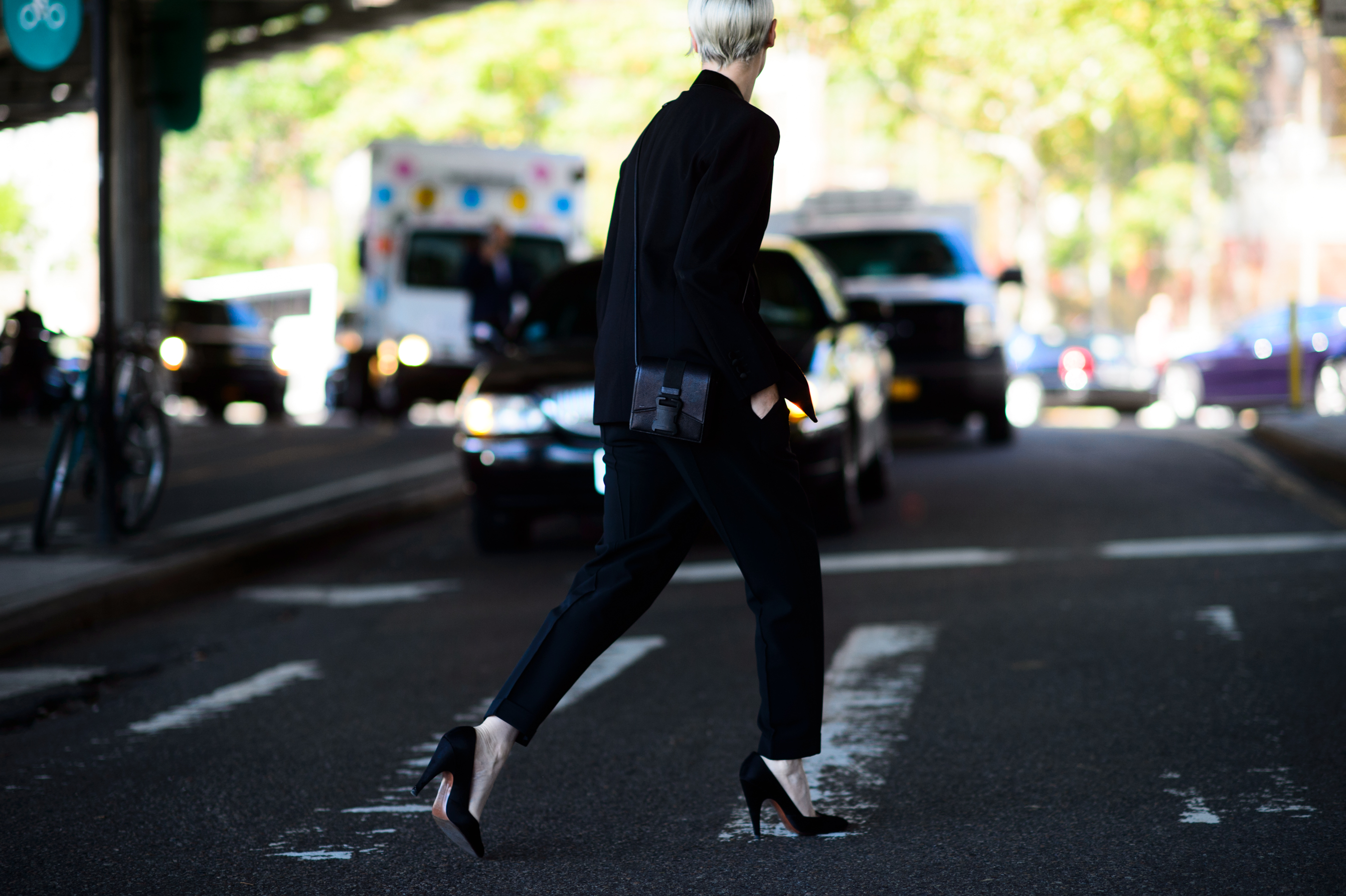 Woman in black suit and shoes crosses the road