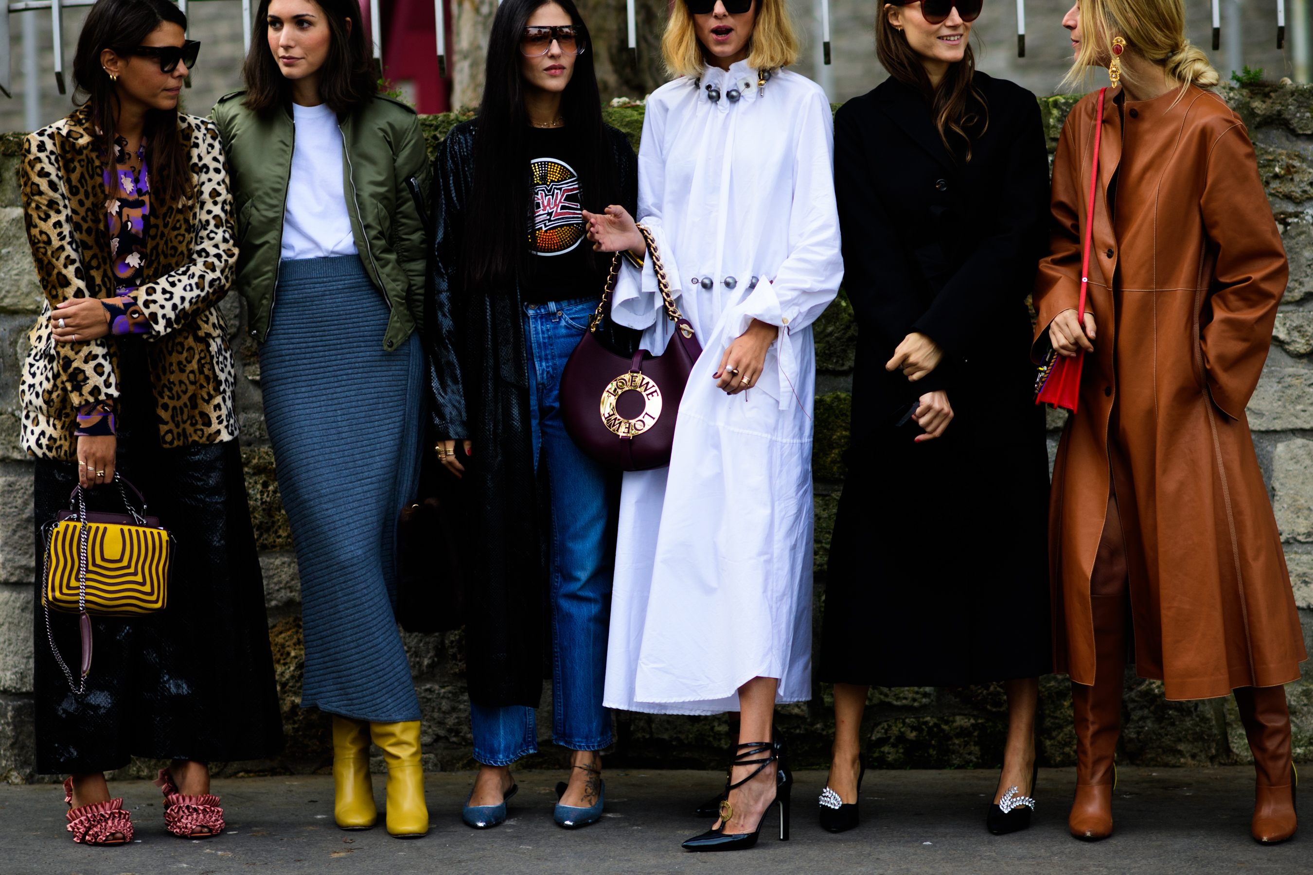 Six women stood against wall wearing long coats