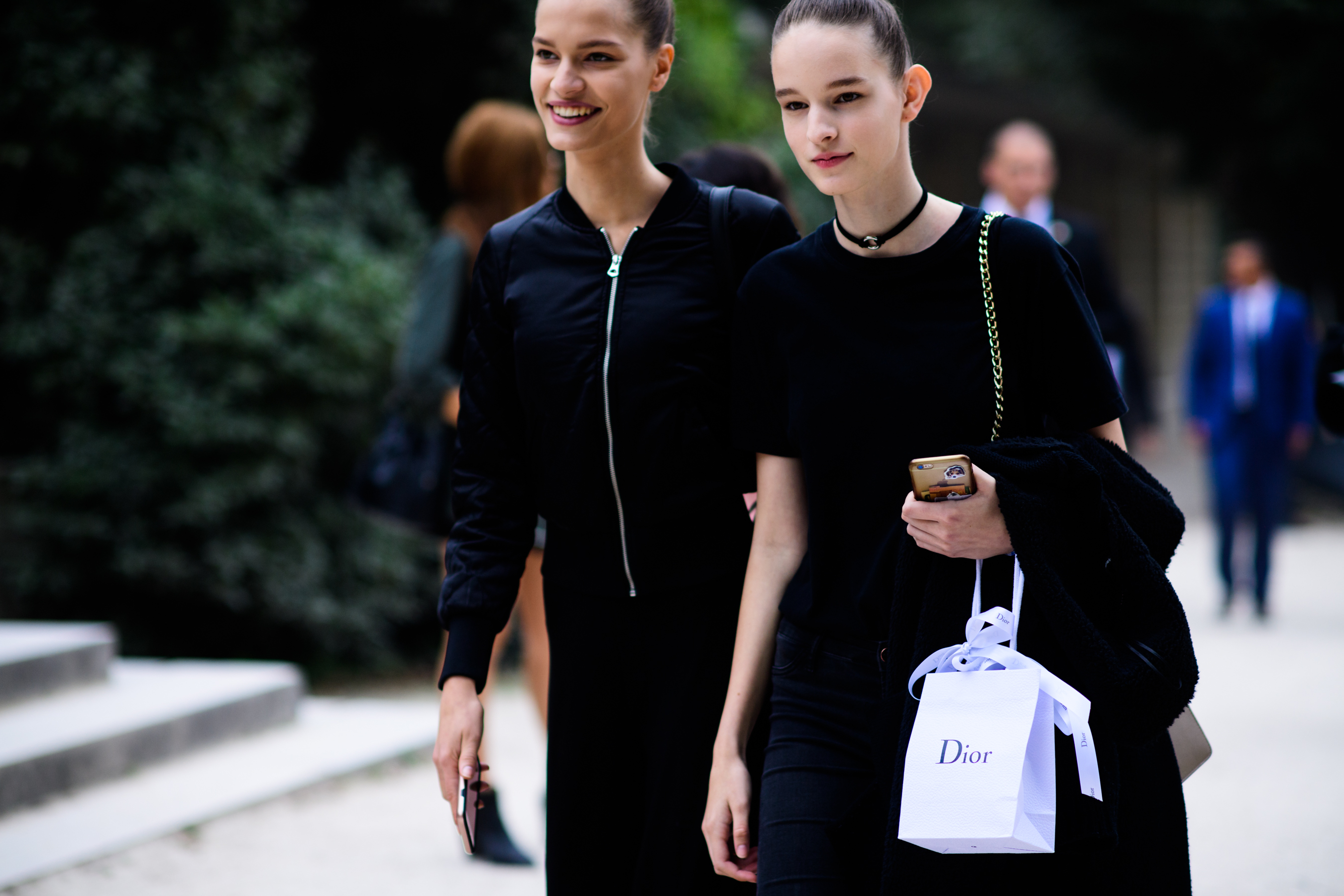 Two models walking in black outfits with bags