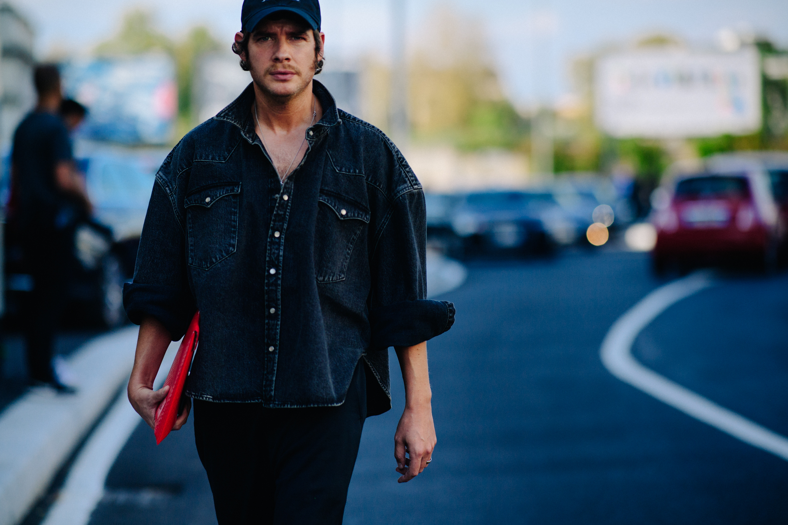 Man wearing black denim shirt holding red bag