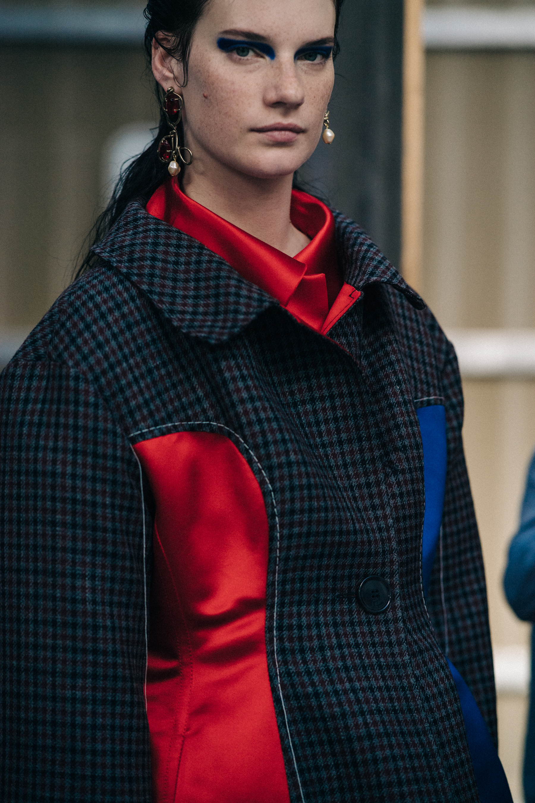 Model backstage wearing a red shirt under a coat